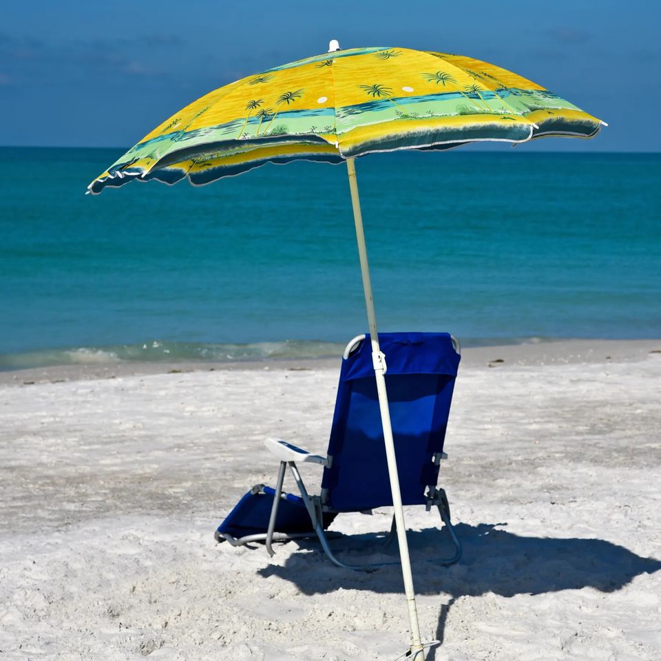 Blue beach chair under a yellow umbrella on white sand by the water for beach chair rentals