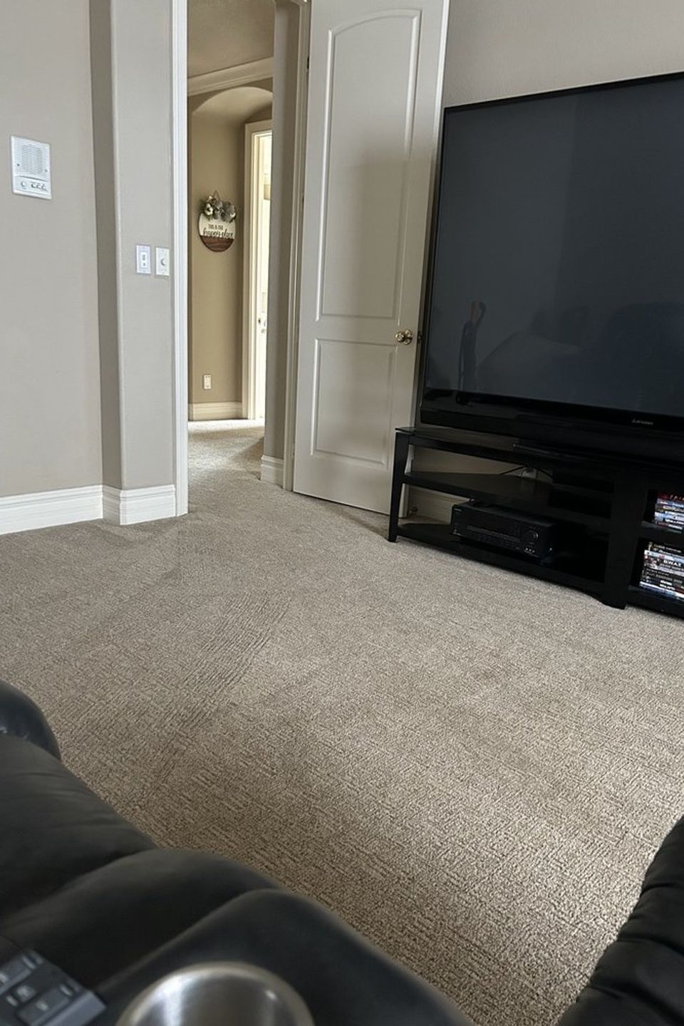 Cozy living room with beige carpet, black recliner, flat‑screen TV on media stand, and hallway leading to adjacent room