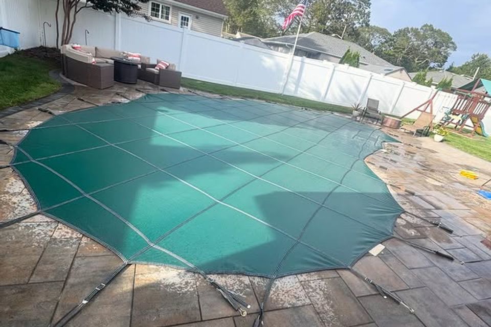 Green mesh safety cover secured over an inground pool on a paver patio in Long Island NY