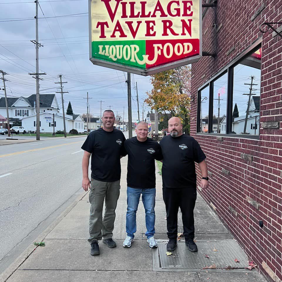 Three owners standing outside Village Tavern under the hanging sign on a city street