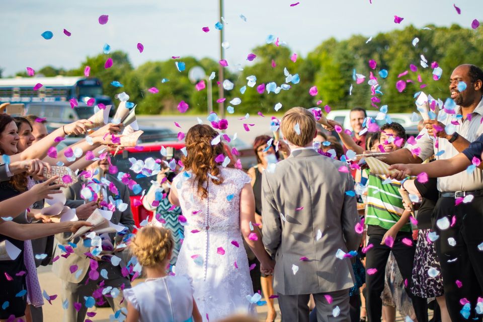 Couple walking while guests cheer and throw confetti. 