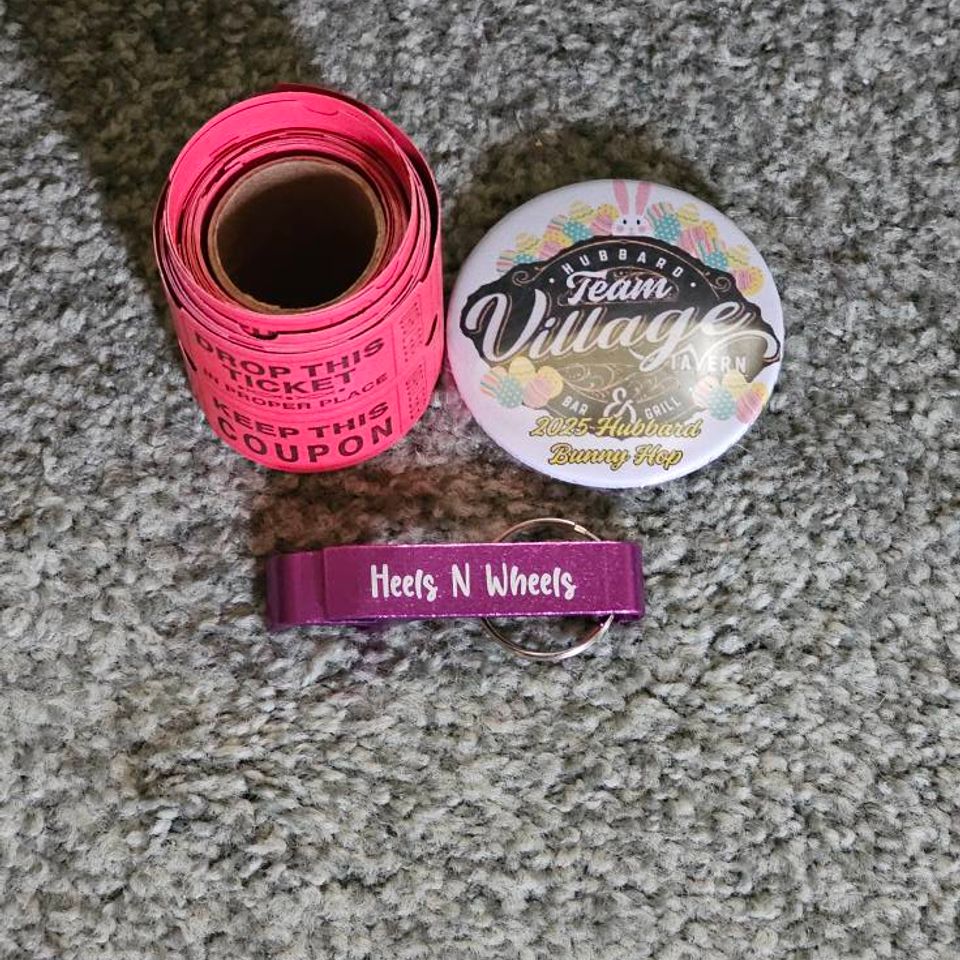 Raffle ticket roll, event button, and Heels N Wheels keychain displayed on a carpeted surface.