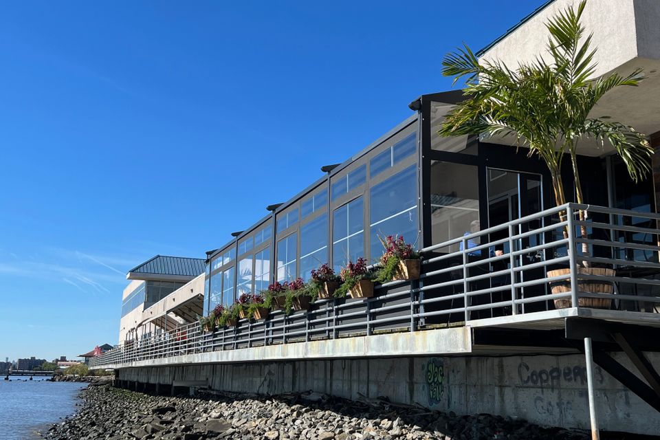 Glass paneled winter enclosure with a black aluminum frame running the length of a waterfront restaurant deck