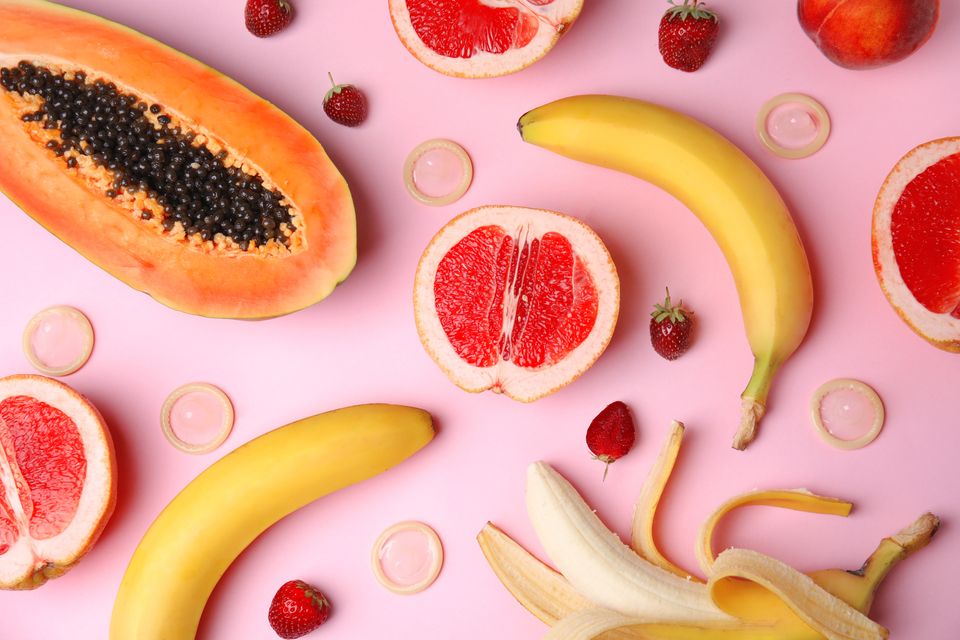 Playfully arranged bananas  papaya  and citrus fruits on a pink background  visually representing sex education themes.