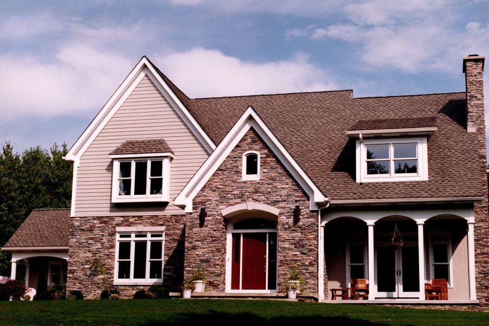 Two-story custom home with a stone and siding exterior, covered front porch, arched entryway, and professionally landscaped yard.