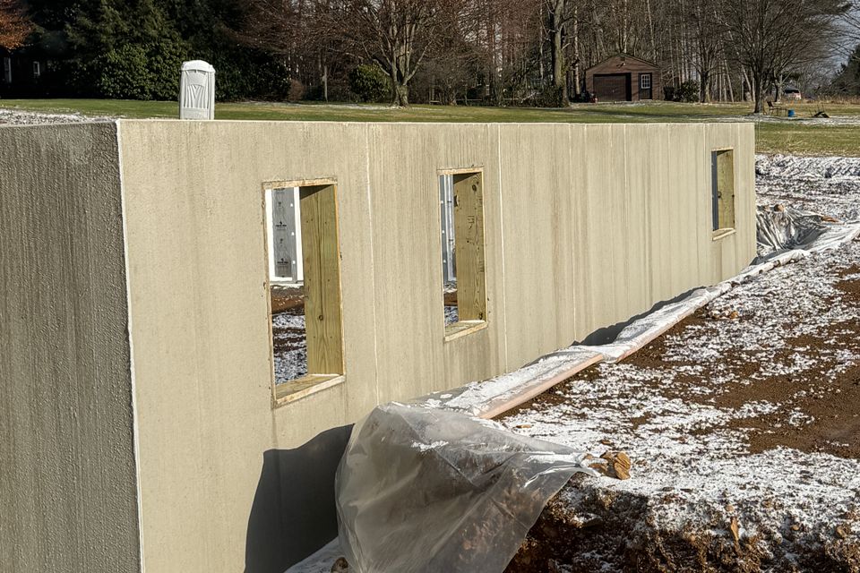 Concrete foundation under construction for a residential home addition with framed window openings and site preparation in progress.