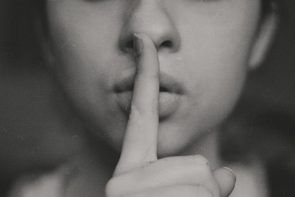 Black and white photo of nose down face with a finger pressed to their lips like "Shhhhh." 
