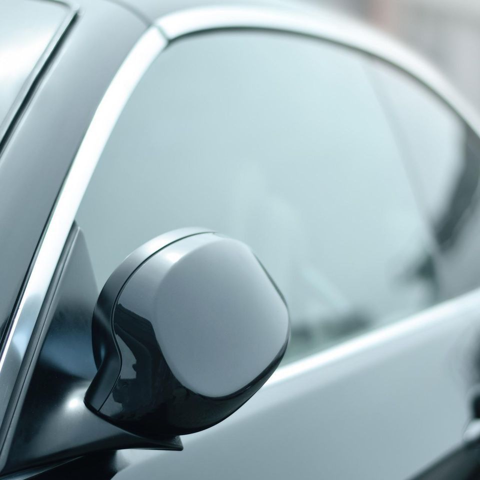 Close-up of a vehicle side mirror and window representing insurance-covered auto glass repair and replacement services.
