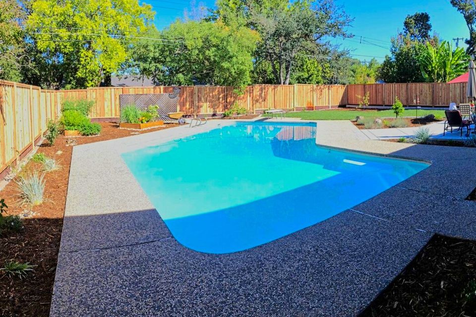 Outdoor pool surrounded by concrete patio, plants, and enclosed wooden fence