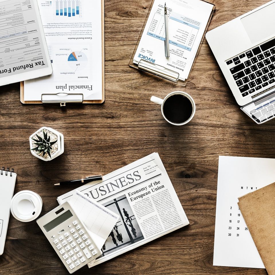 Top-down view of a wooden office desk with a laptop, financial plans, and business documents—Professional project management and administrative planning for Alta Vista Landscaping & Tree Service.
