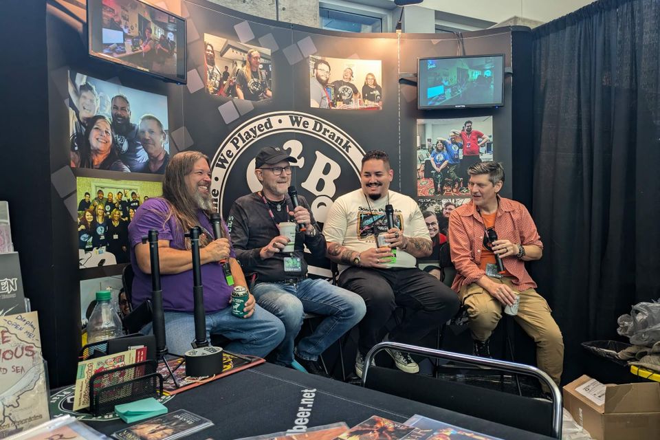 Four panelists speaking into microphones during a live podcast recording at the 3 Beers and a Mic booth at GameHoleCon