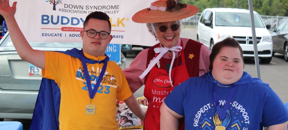 Two Buddy Walk participants posing with a community volunteer dressed as Mrs. Claus during the event.