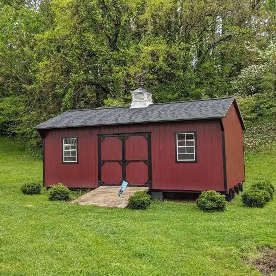 Red Quaker shed with cupola, black trim and wood ramp on an Elizabethton TN lawn