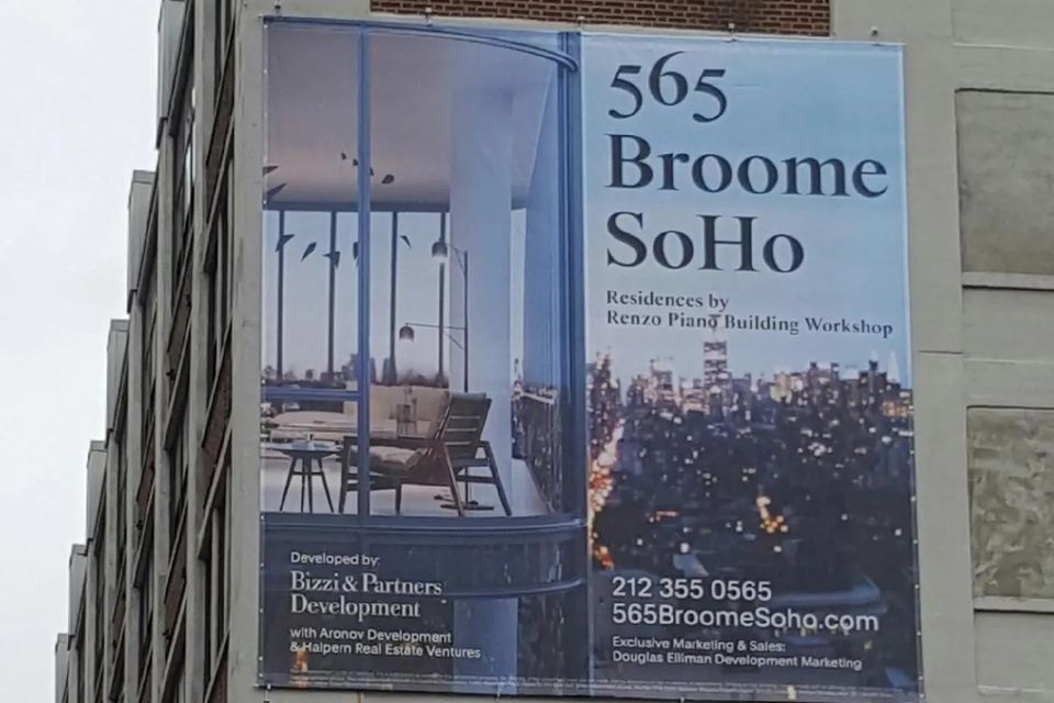 Printed large-format graphic panels wrapping a construction site hoarding along a Manhattan sidewalk