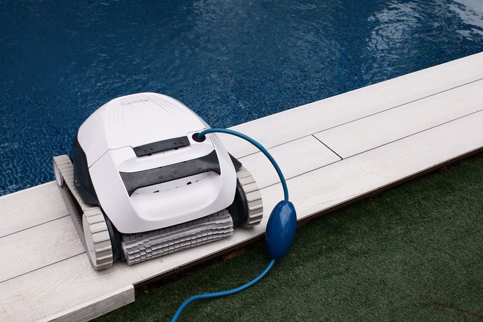 Robotic pool cleaner sitting on the deck beside a pool after cleaning