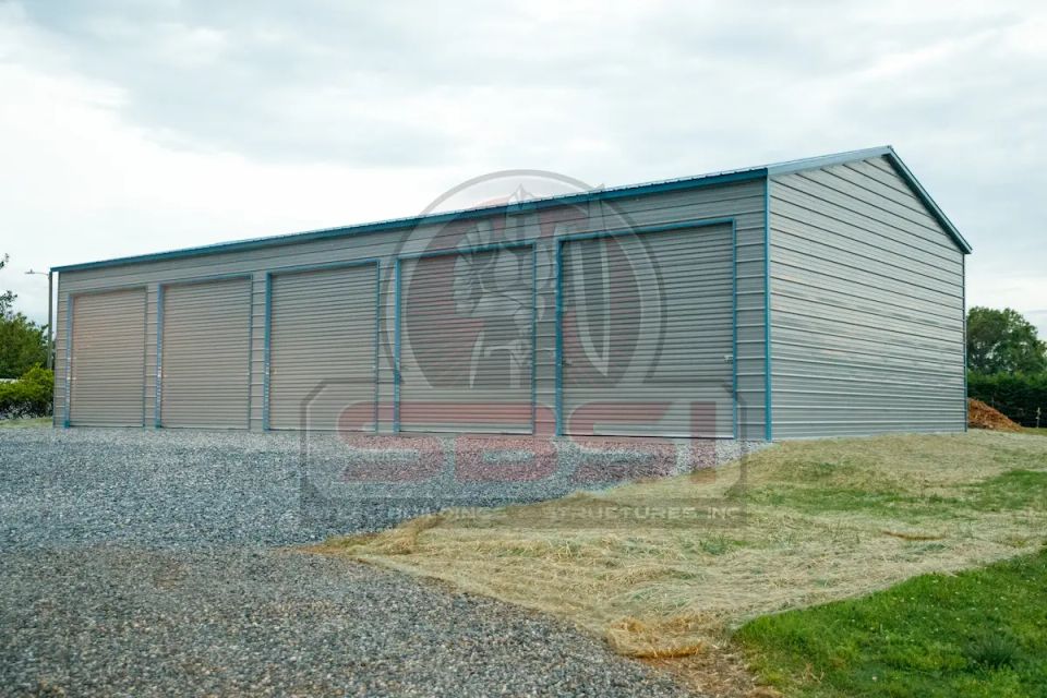 Gray and teal steel garage with multiple roll up doors on gravel lot with SBSI watermark representing steel garages in Alabama