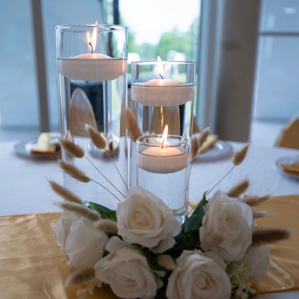 Floating candle and white rose centerpiece on a gold satin runner at a styled reception table