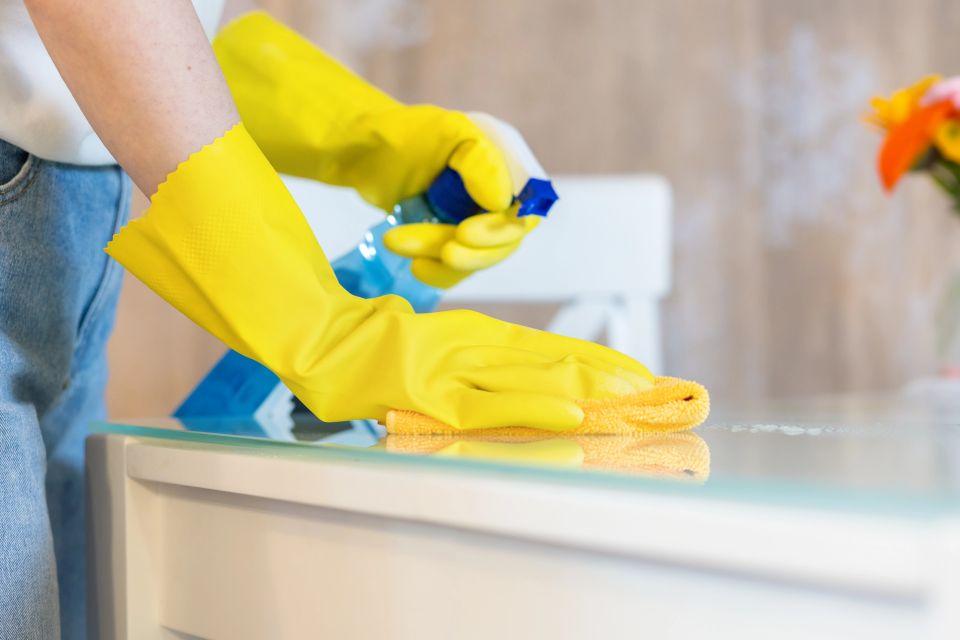A cleaning lady with yellow cleaning gloves wiping down a table with a cleaning solution spray