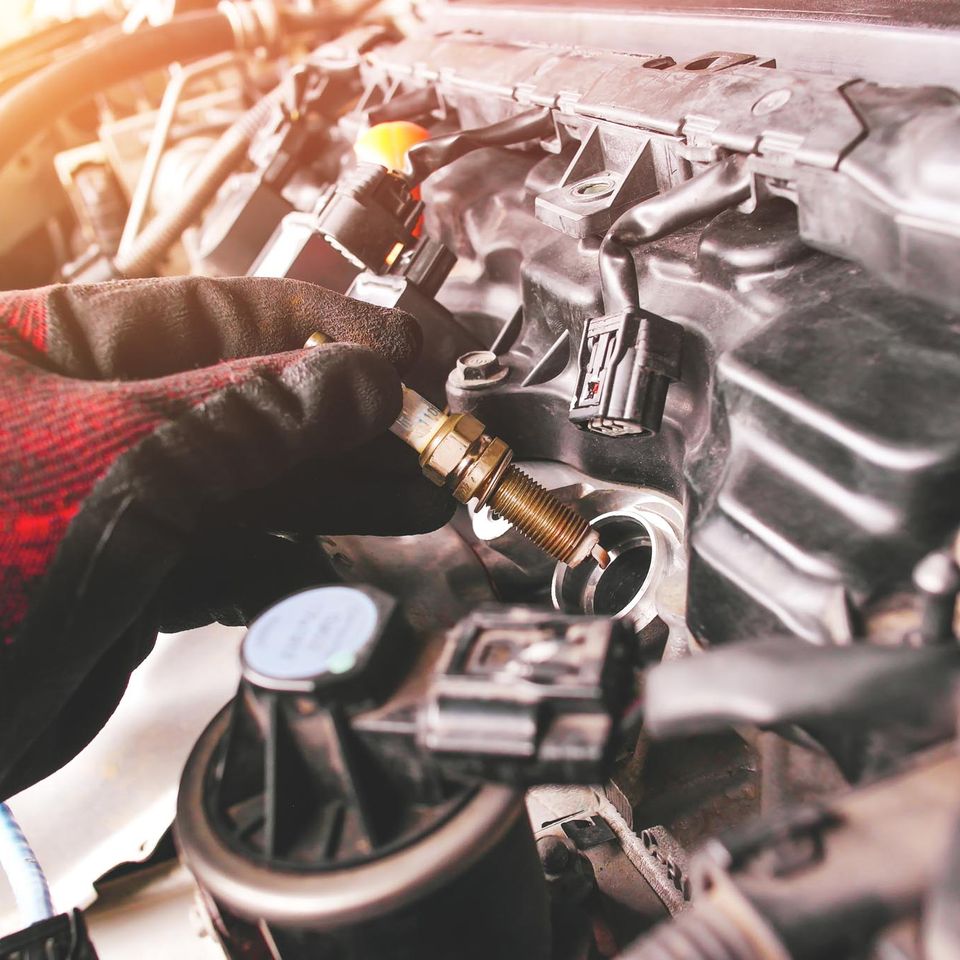 Bedford auto repair auto mechanic is installing automobile iridium spark plugs into ignition socket engine block engine compartment