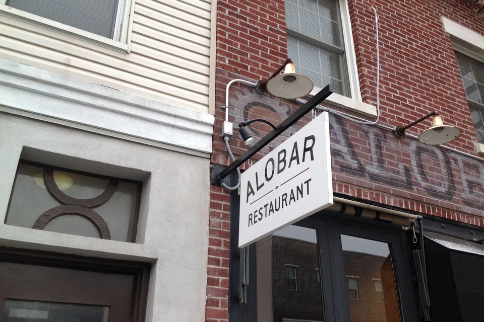 White double faced blade sign for Alobar Restaurant projecting from a brick storefront