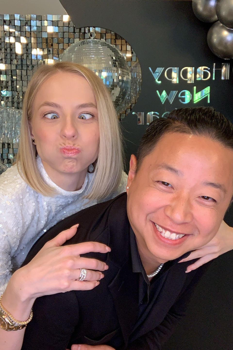 Couple taking a fun selfie at an event with a photo booth backdrop.