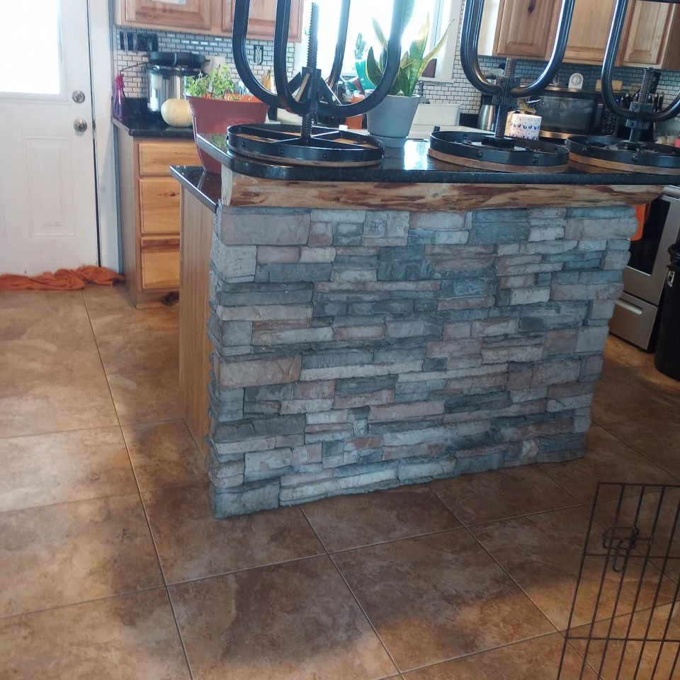 Kitchen island featuring gray veneer stone with a wood countertop and bar seating.