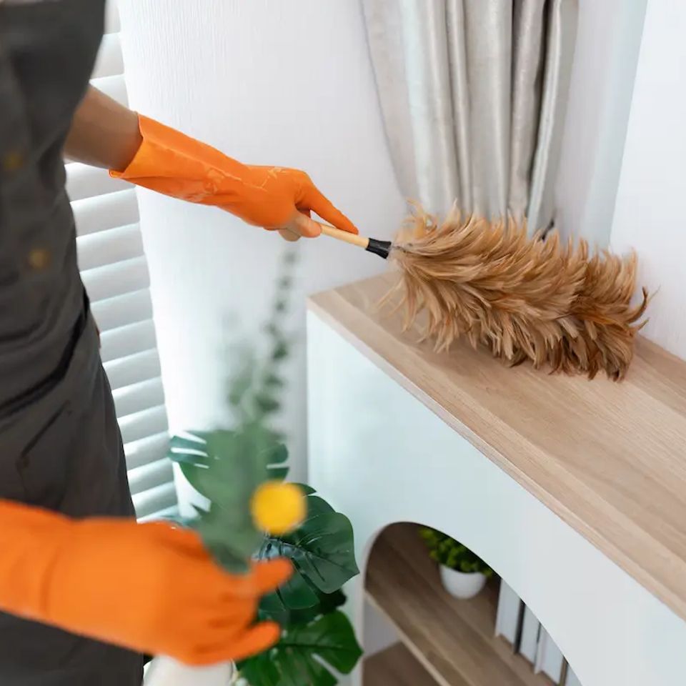 Housekeeper in orange gloves dusting wooden shelf during house cleaning service in Virginia Beach VA