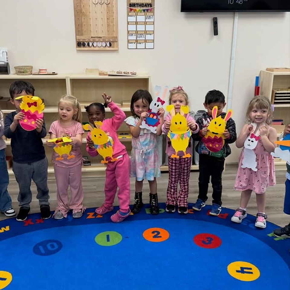 Preschoolers holding handmade spring craft projects on the classroom rug at a Montessori school in Palmdale CA