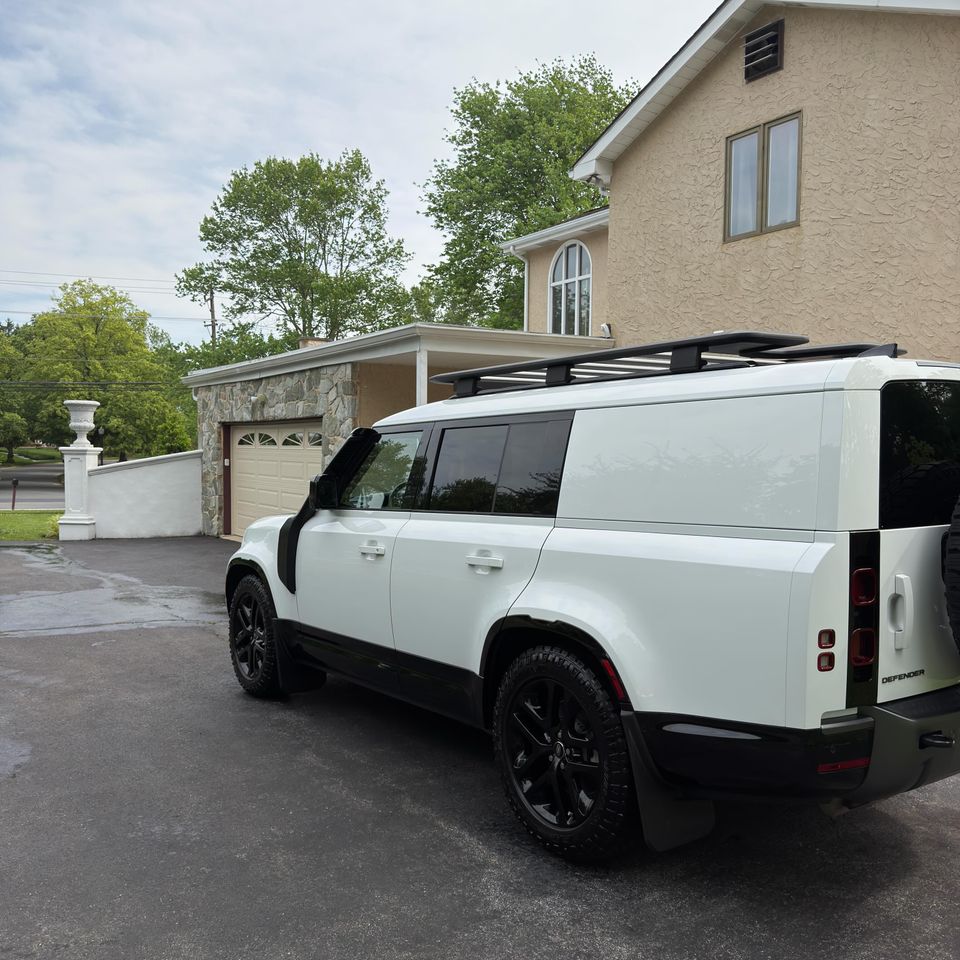 Rear three-quarter view of a freshly washed white Land Rover Defender with black wheels and roof rack
