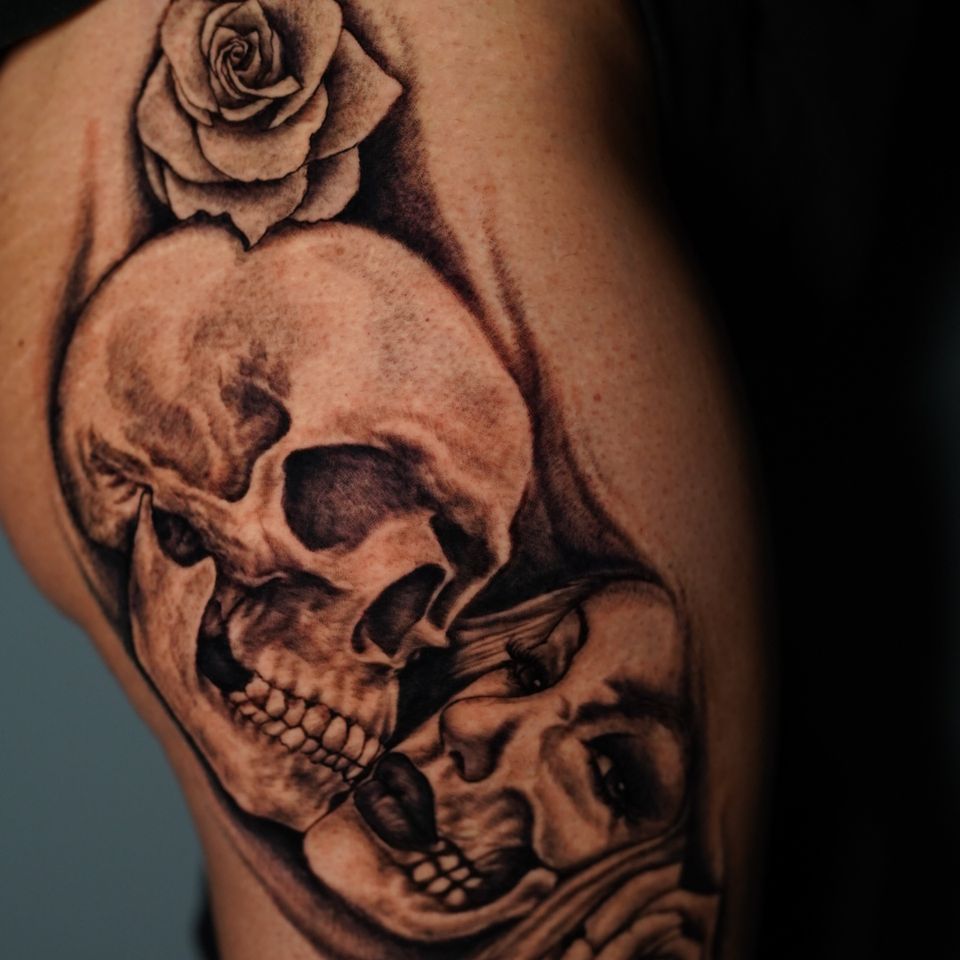 Image of a skull and a womans face with only partial skull showing in black ink and a flower on each side of the tattoo
