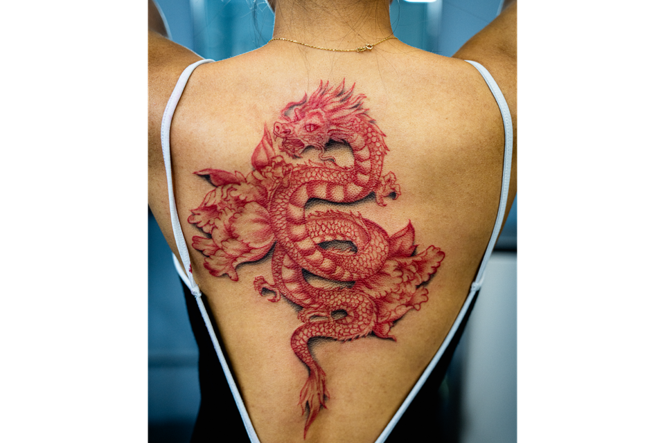 Image of a very detailed dragon tattoo on a woman's back in red ink
