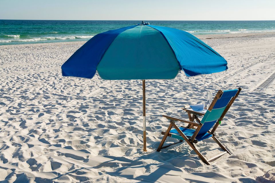 Wooden beach chair under a blue umbrella on white sand facing the Gulf in Destin FL
