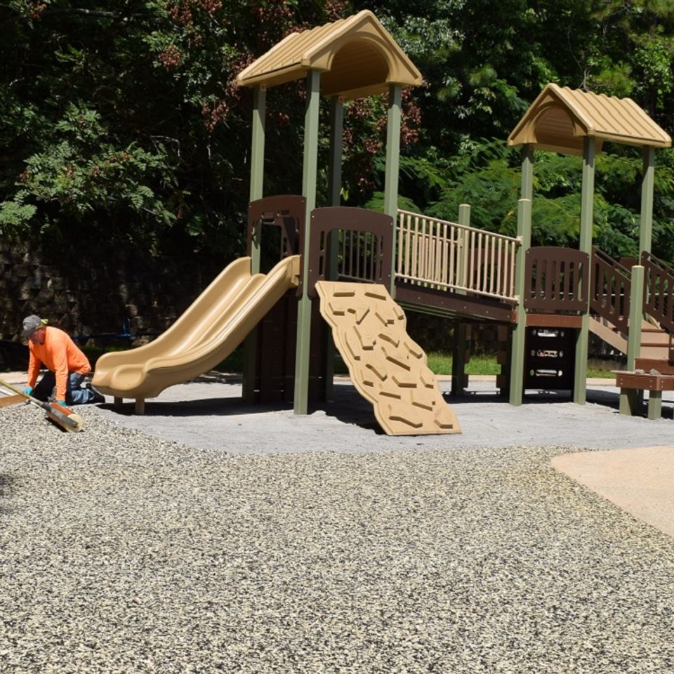 Workers installing an EverStone Flex surface around a playground with slides and play equipment.