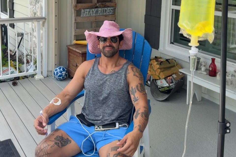 Man in a pink hat receiving a mobile IV drip on a home front porch in Palm Beach County FL