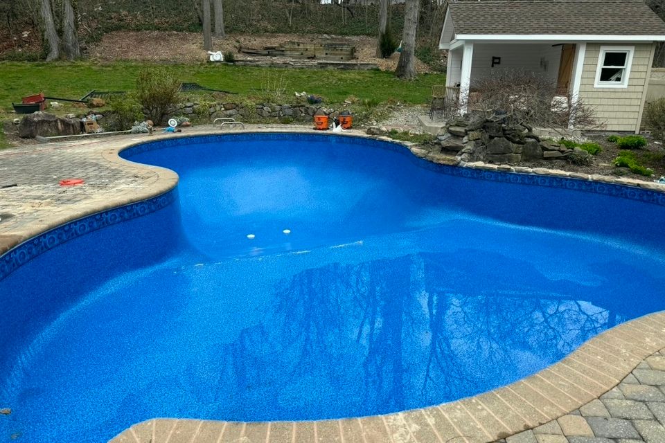 Freeform inground pool with fresh blue liner and paver coping filled after a liner replacement in Long Island NY