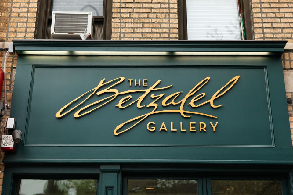 Gold script and block dimensional letters on a dark green storefront panel, lit by a cove light above