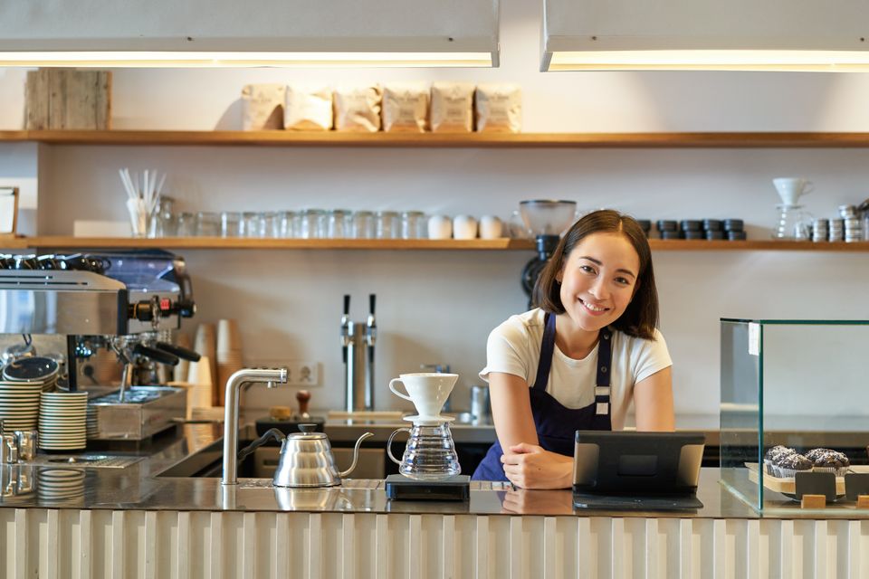 Happy smiling asian barista girl counter working with pos terminal brewing filter kit mak