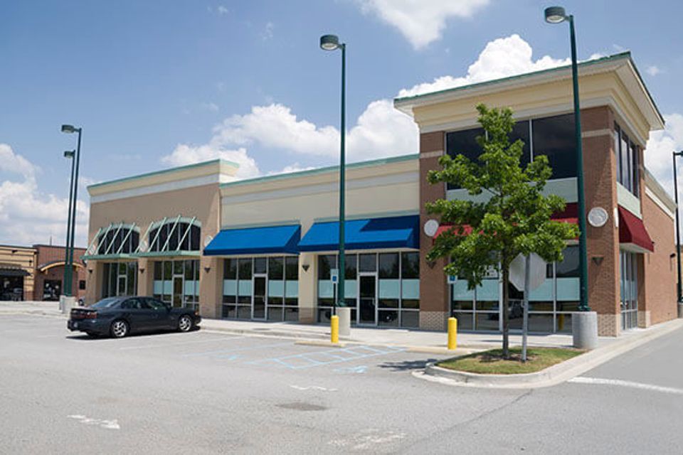 row of retail stores with parking lot and a car