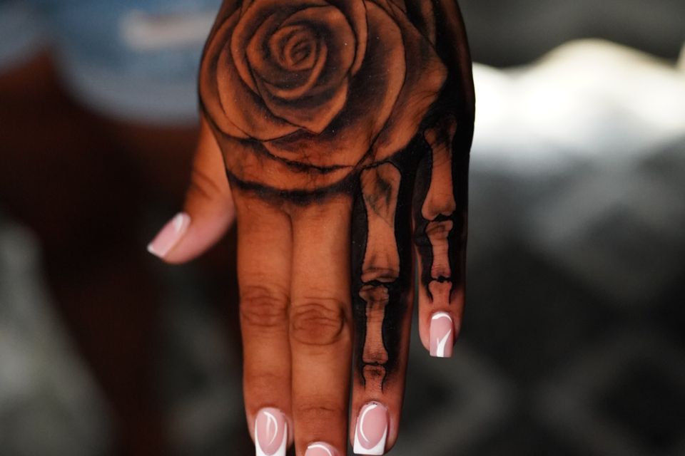 Image of a rose tattoo and bones on finger like an x-ray and the word "Blessed" above in black & grey