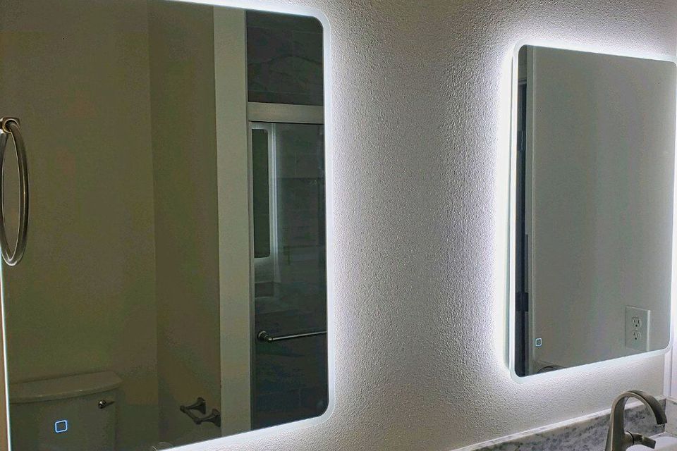 A pair of modern, rectangular bathroom vanity mirrors with integrated LED backlighting installed over a marble double-sink vanity