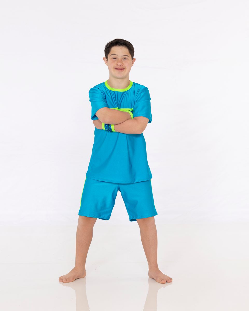 Portrait of a smiling young person with Down syndrome standing with arms crossed against a white background.