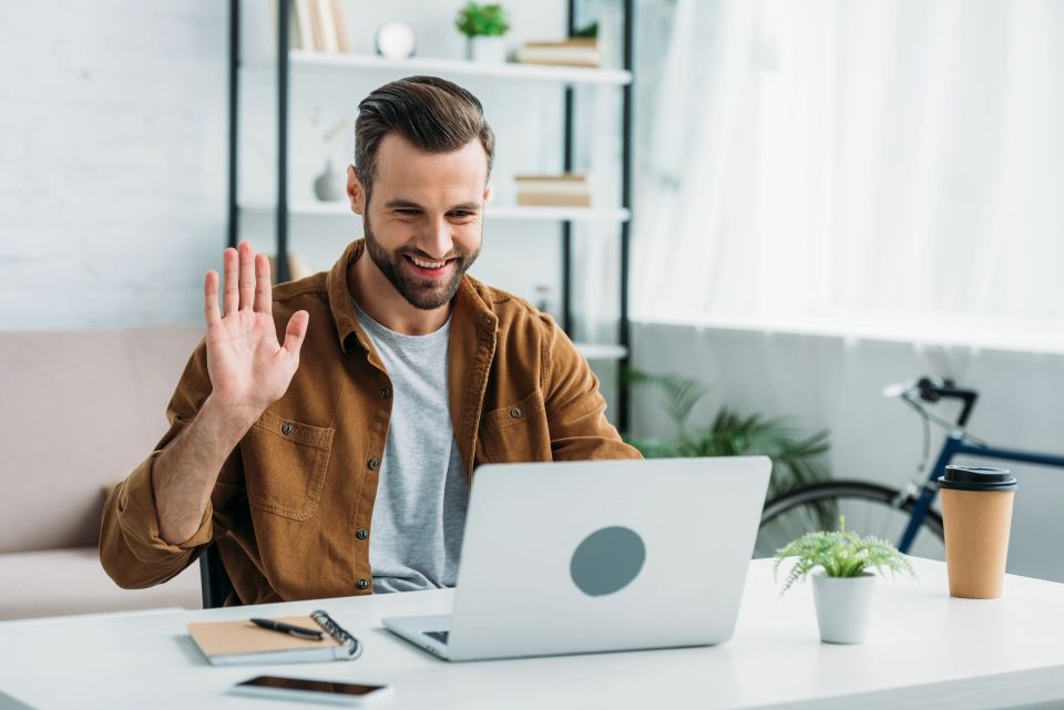 Man waving at a laptop during a virtual check in for online fitness coaching