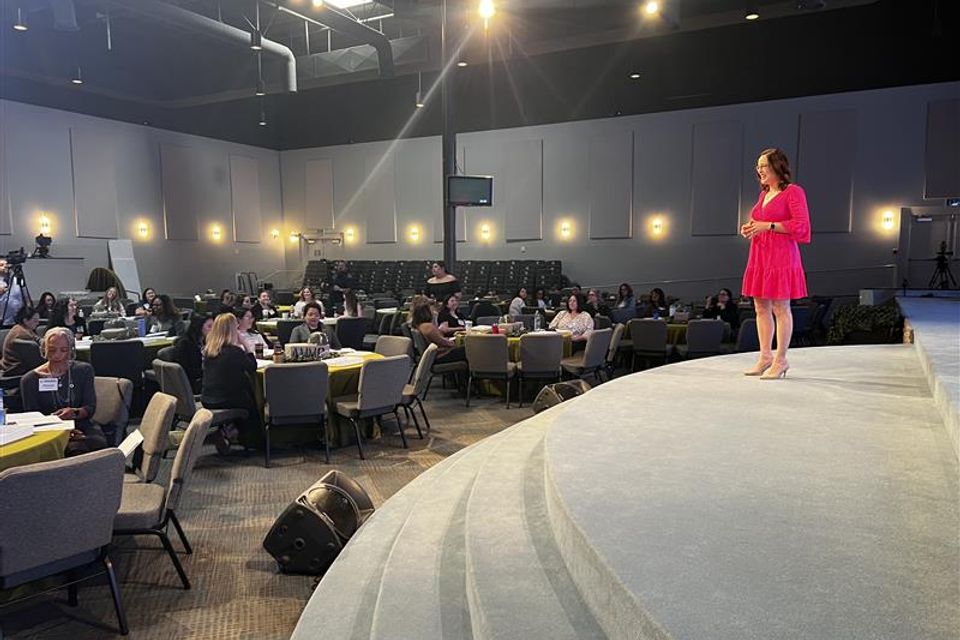 Woman standing on stage speaking to group