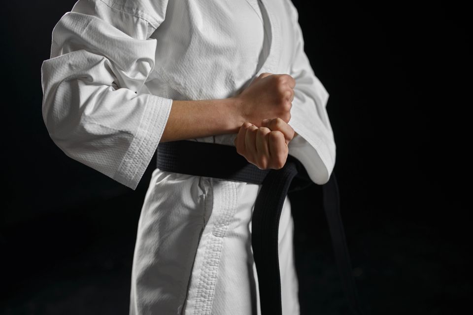A black belt karate student in uniform standing in a combat stance with a black background