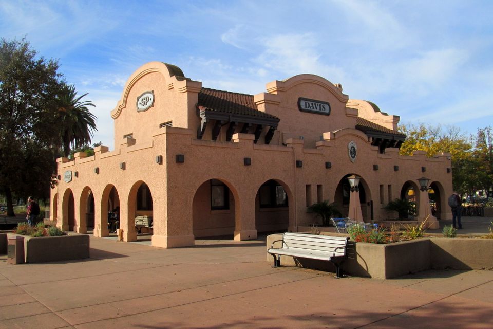 Historic Davis Amtrak train station with Spanish-style architecture, arched doorways, and tiled roof under clear skies