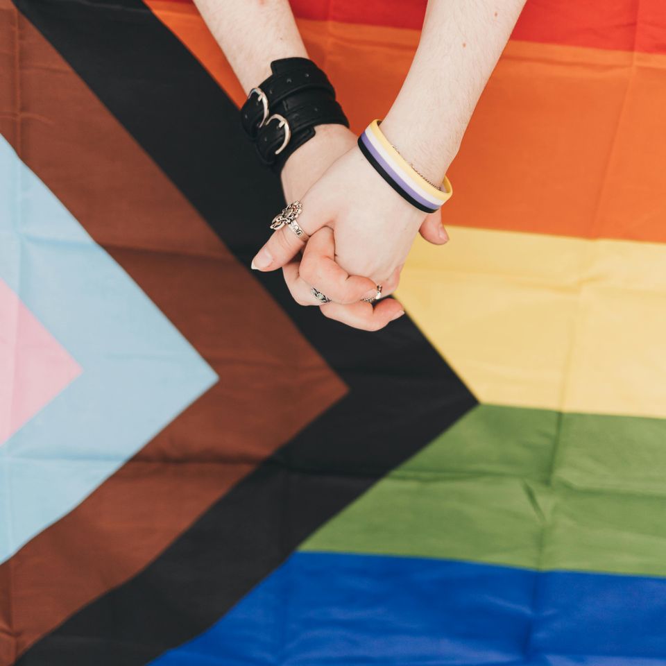 Two people holding hands in front of the pride flag