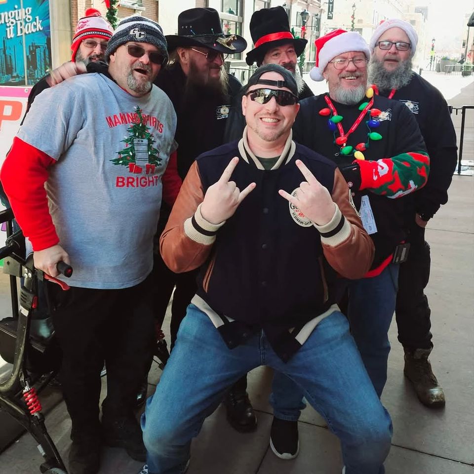 Group of attendees wearing Christmas hats, sweaters, and holiday accessories posing for a photo on a city sidewalk.