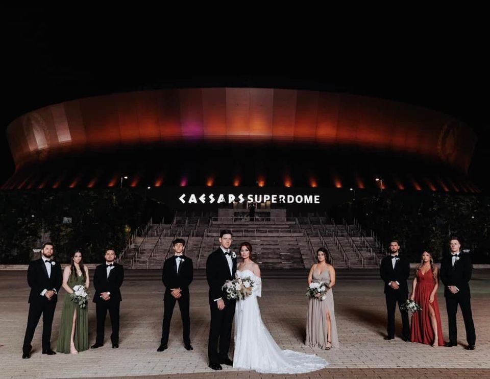 Wedding couple and bridal party posing in front of the Caesars Superdome at night.