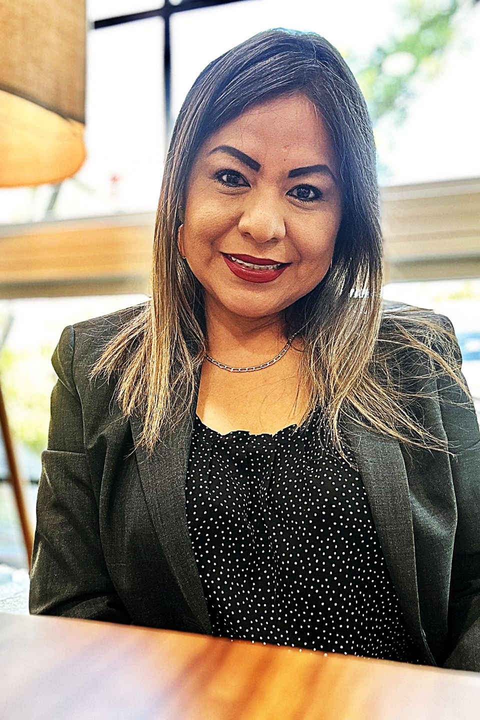 Nancy delgado owner nadel design houston wearing a black blouse with white dots and a gray green jacket min