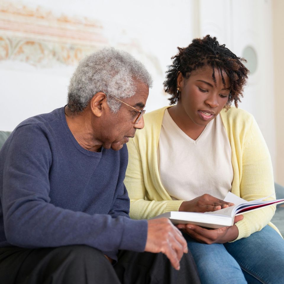 A Woman Reading a Book while Sitting Beside the Man in Blue Sweater